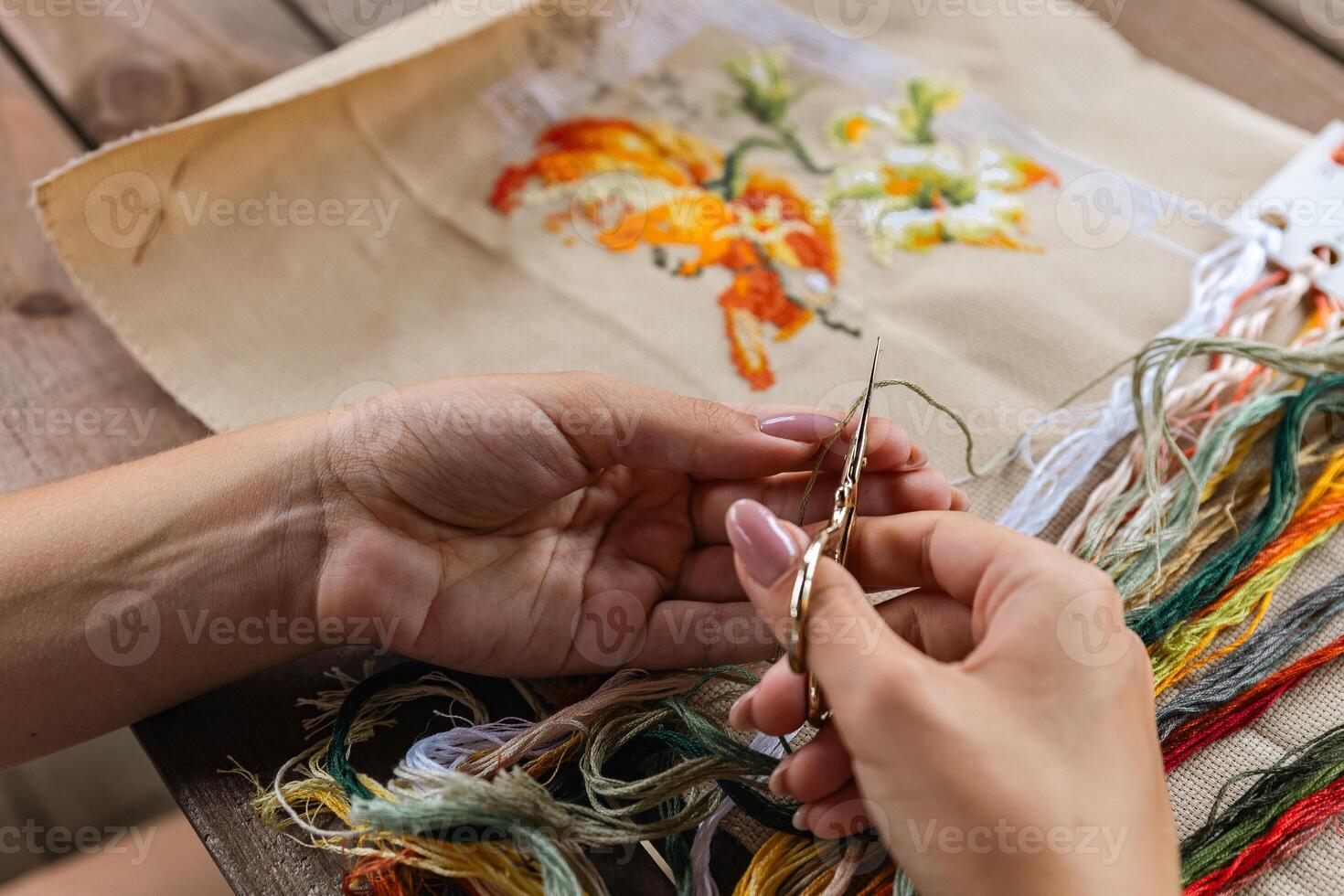 A hand holding embroidery scissors about to cut a thread. A hand with scissors cuts the thread. Close-up of cross stitch. Crafts and embroidery. photo