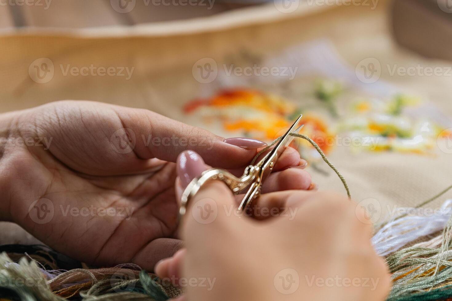 A hand holding embroidery scissors about to cut a thread. A hand with scissors cuts the thread. Close-up of cross stitch. Crafts and embroidery. photo