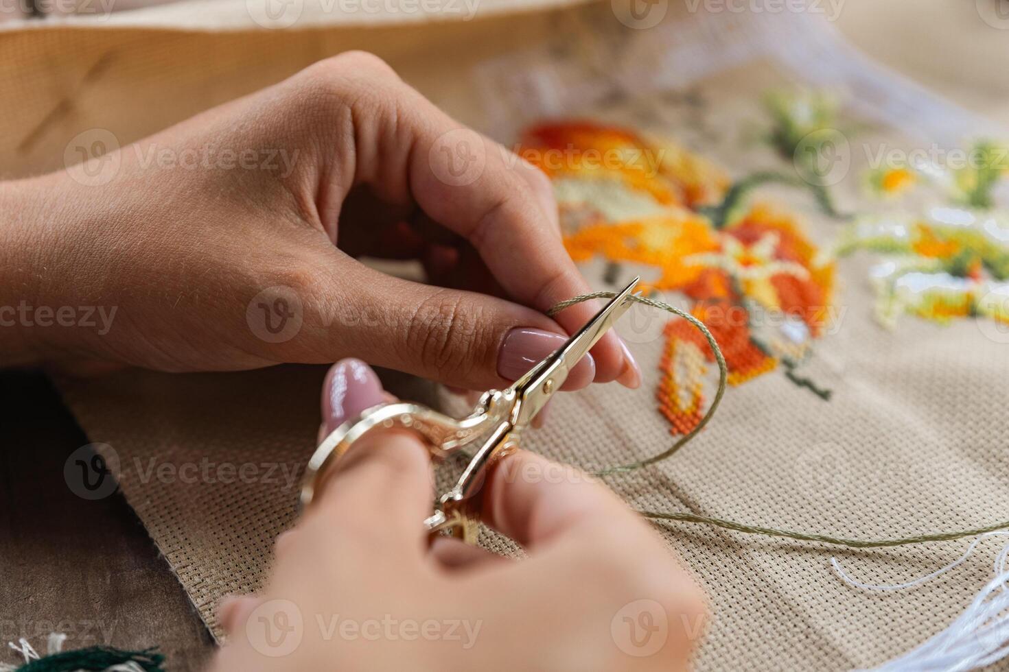 A hand holding embroidery scissors about to cut a thread. A hand with scissors cuts the thread. Close-up of cross stitch. Crafts and embroidery. photo