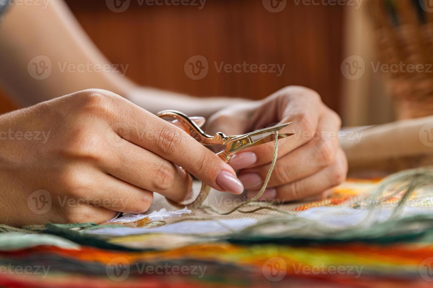 A hand holding embroidery scissors about to cut a thread. A hand with scissors cuts the thread. Close-up of cross stitch. Crafts and embroidery. photo