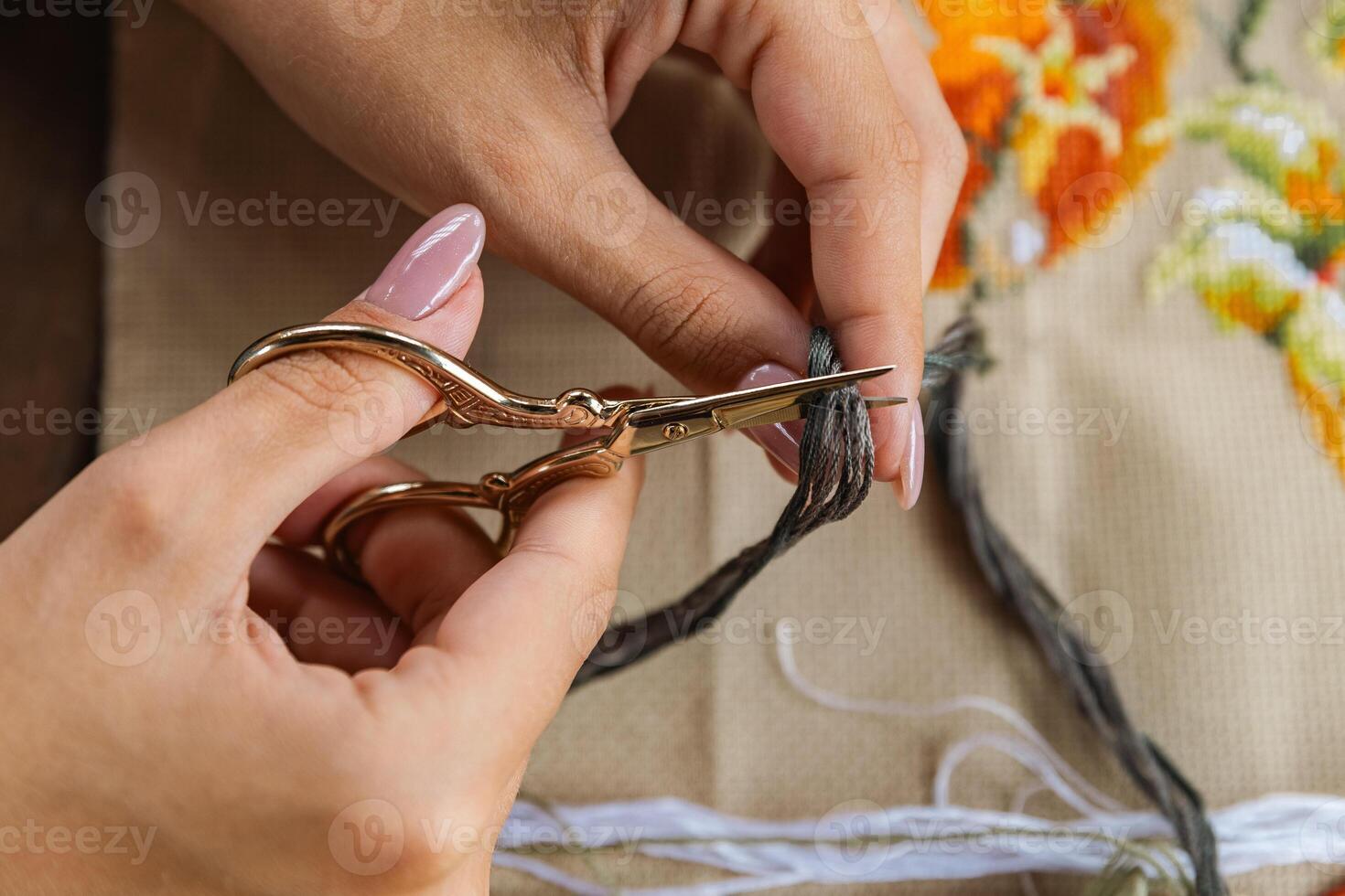 A hand holding embroidery scissors about to cut a thread. A hand with scissors cuts the thread. Close-up of cross stitch. Crafts and embroidery. photo