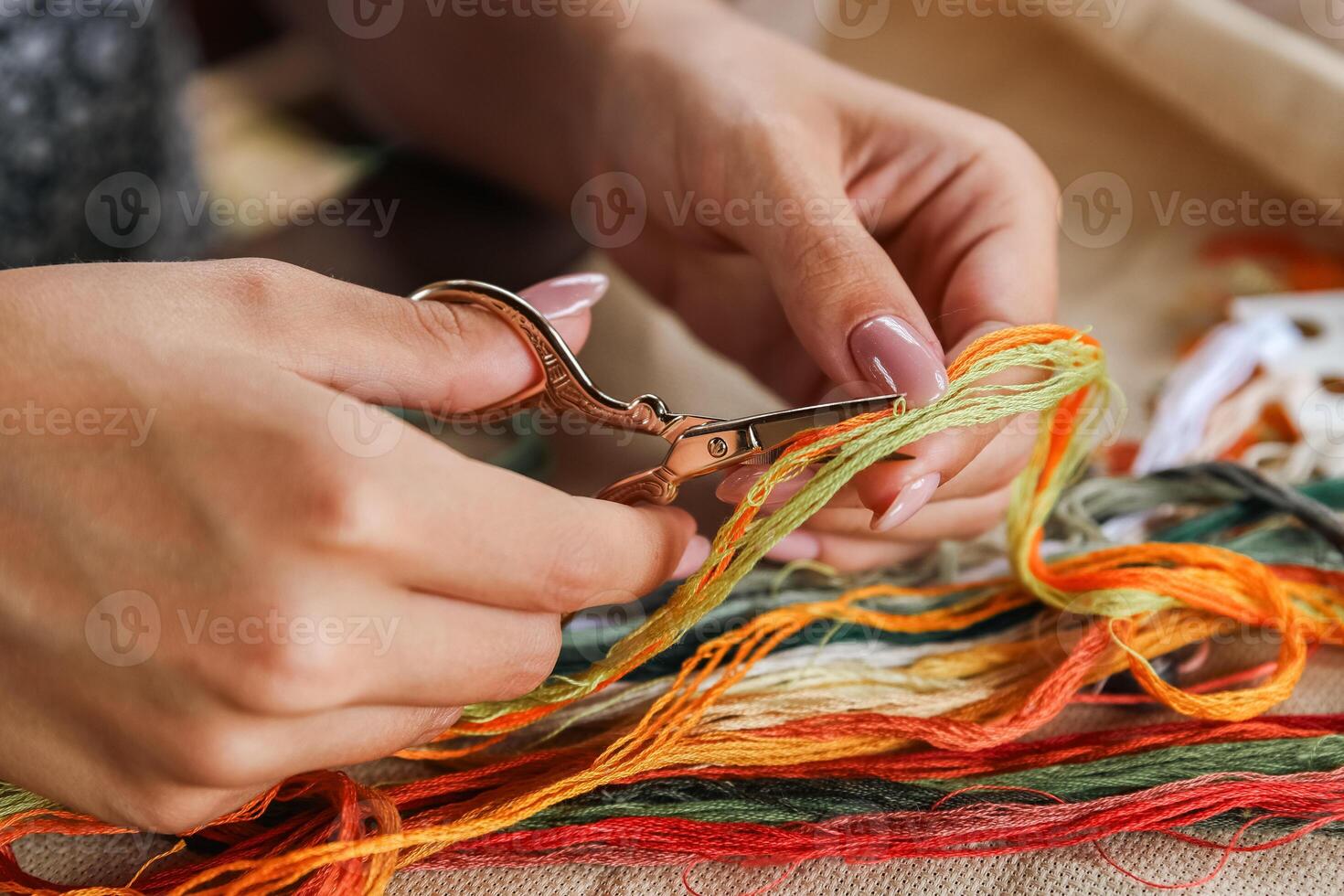 A hand holding embroidery scissors about to cut a thread. A hand with scissors cuts the thread. Close-up of cross stitch. Crafts and embroidery. photo