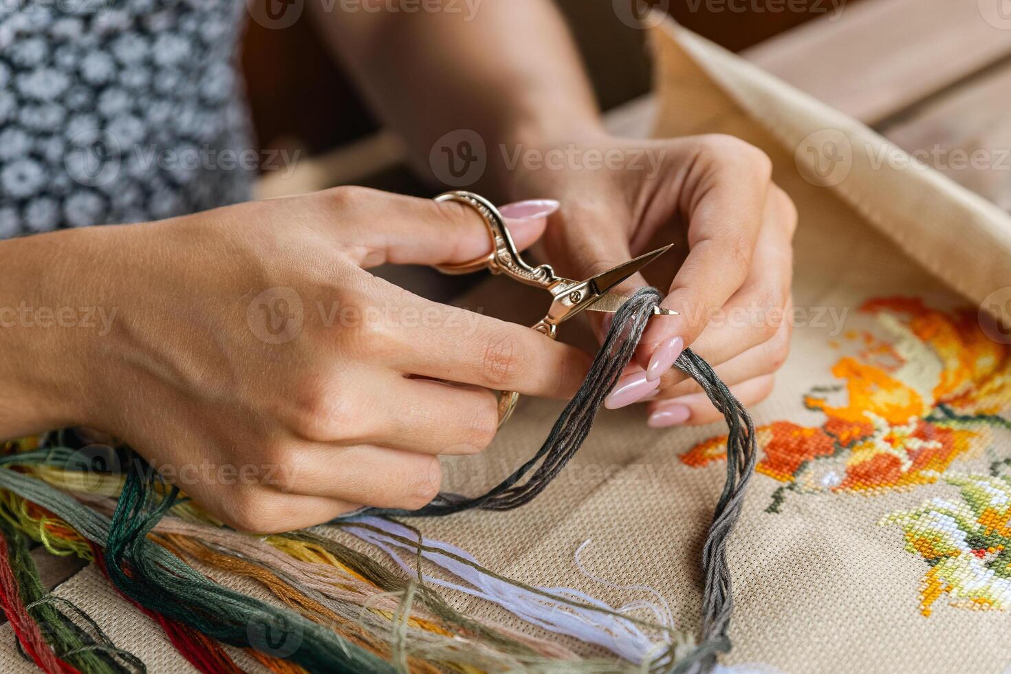 A hand holding embroidery scissors about to cut a thread. A hand with scissors cuts the thread. Close-up of cross stitch. Crafts and embroidery. photo