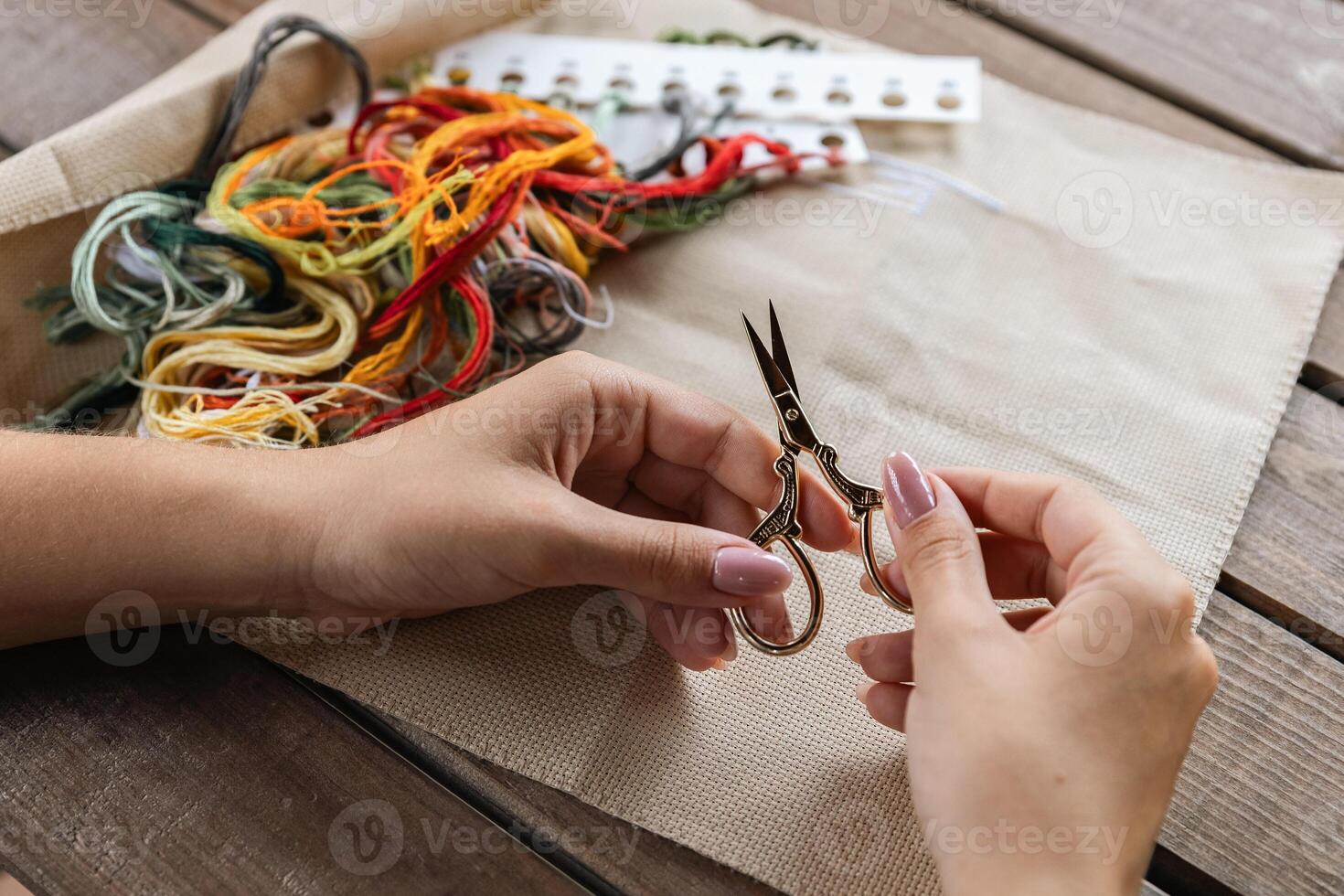 A girl holds needlework scissors in front of threads and embroidery fabric. Crafts and creativity. Cross stitch. photo