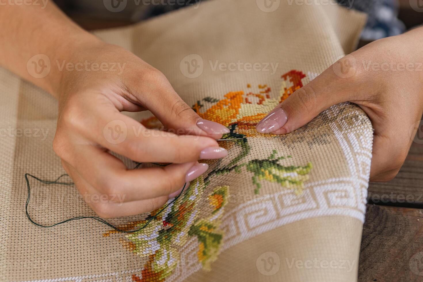 A woman doing cross stitching. Close-up of hands with a needle threading the thread through the fabric. Embroidery of a picture. In the background are colorful embroidery threads. photo