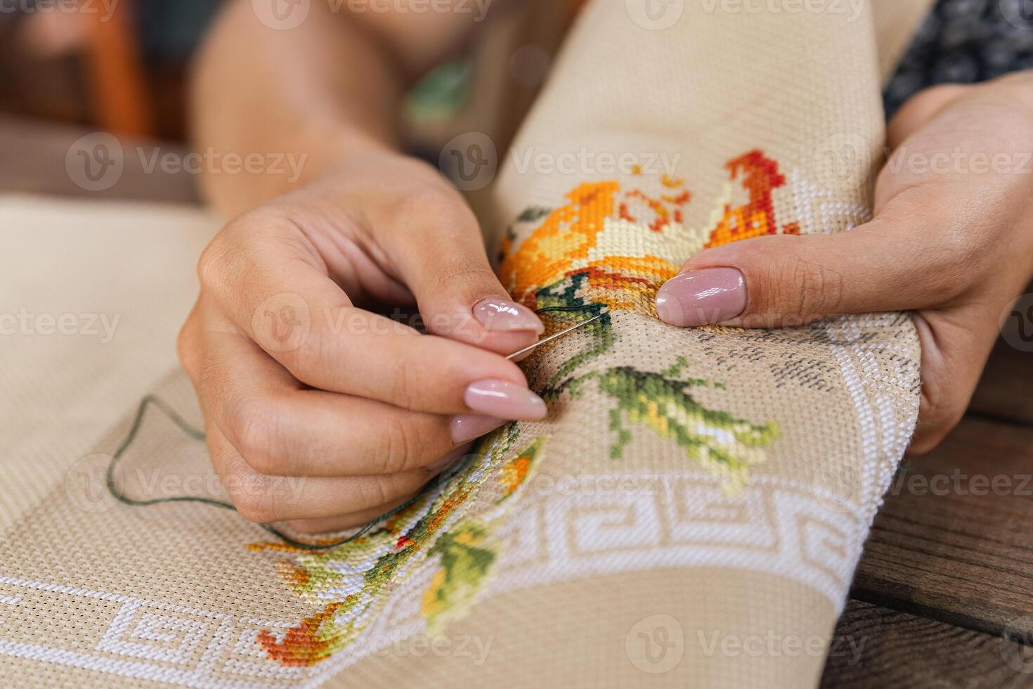 A woman doing cross stitching. Close-up of hands with a needle threading the thread through the fabric. Embroidery of a picture. In the background are colorful embroidery threads. photo