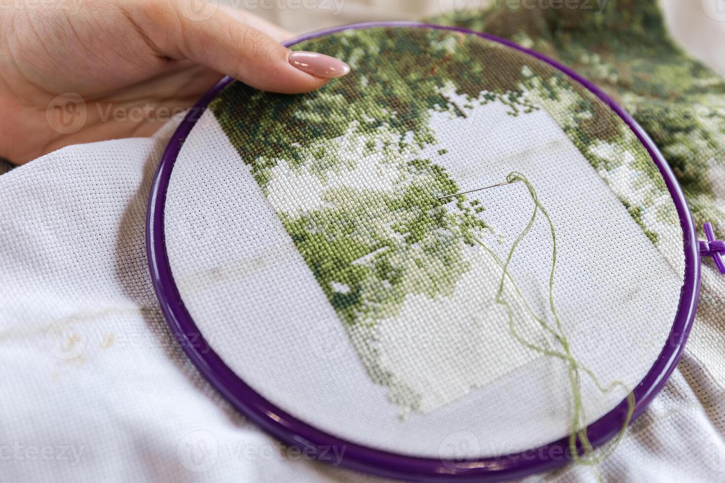 A girl cross-stitching. Close-up of hands carefully maneuvering a needle through the fabric. A purple embroidery hoop holds the fabric. Close-up of hands with a needle threading the fabric. photo