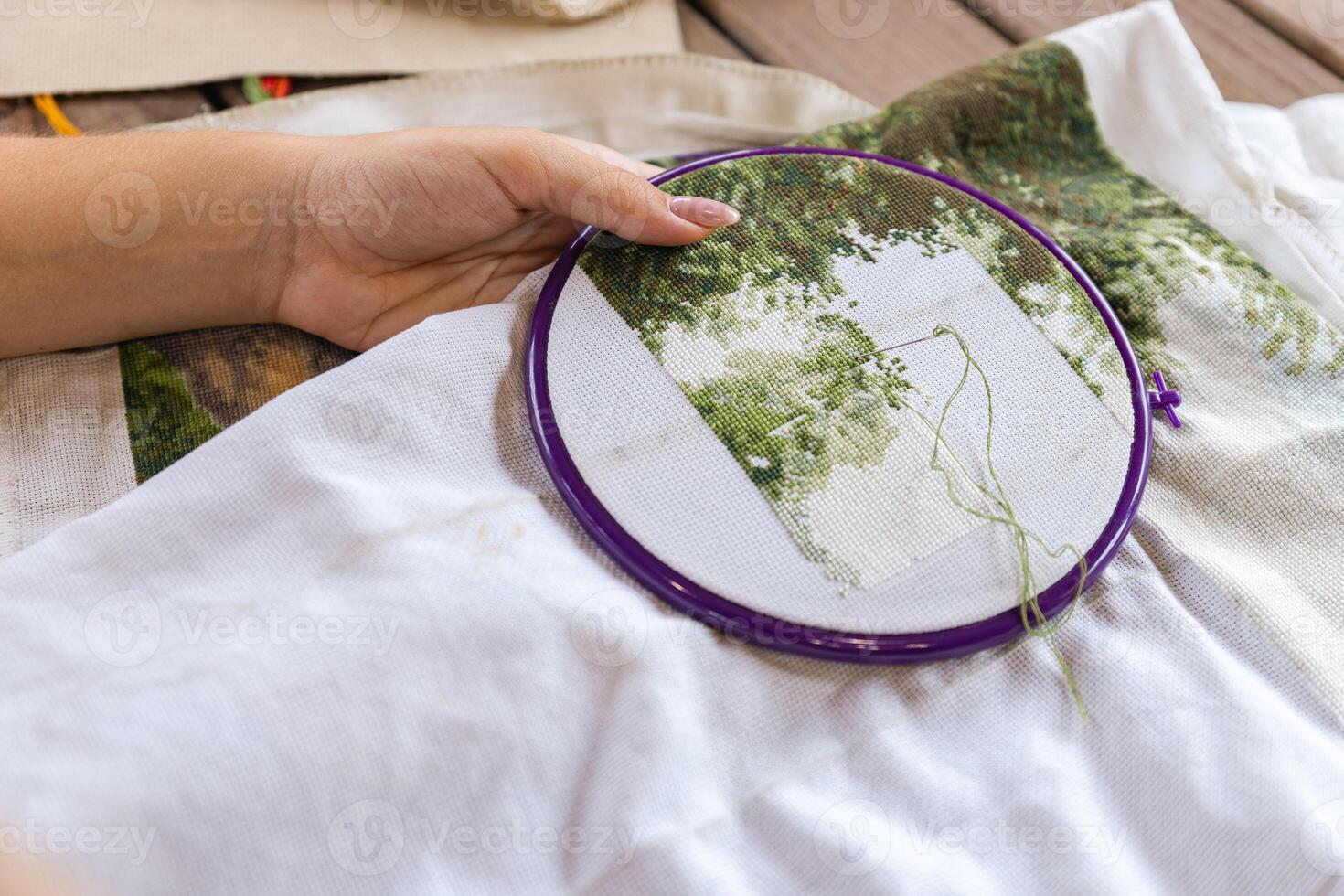 A girl cross-stitching. Close-up of hands carefully maneuvering a needle through the fabric. A purple embroidery hoop holds the fabric. Close-up of hands with a needle threading the fabric. photo