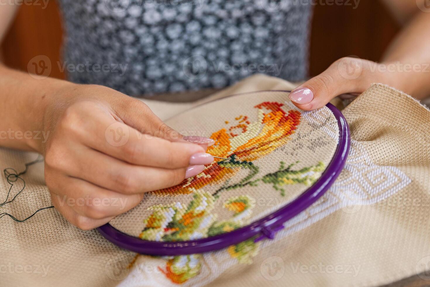 Person engaged in the meticulous process of cross-stitch embroidery. Their hands carefully manipulate the embroidery needle and thread, creating a beautiful floral pattern within the hoop. photo