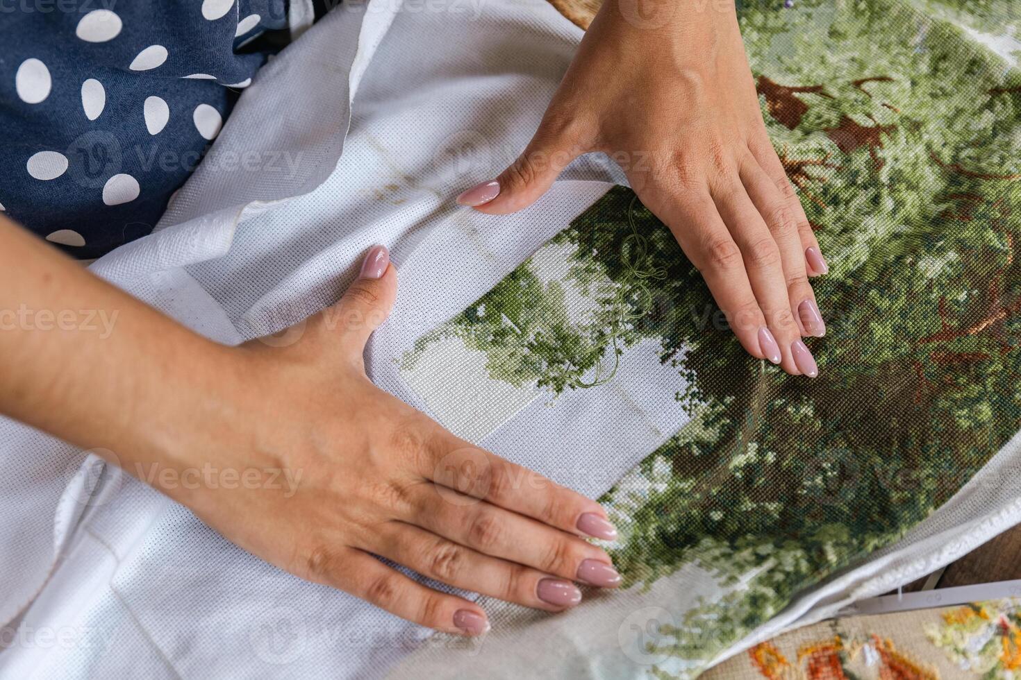 The image shows a person working on a cross-stitch embroidery project. They are using an embroidery hoop to hold the fabric taut and are carefully guiding the needle through the cloth. Hobbies. photo