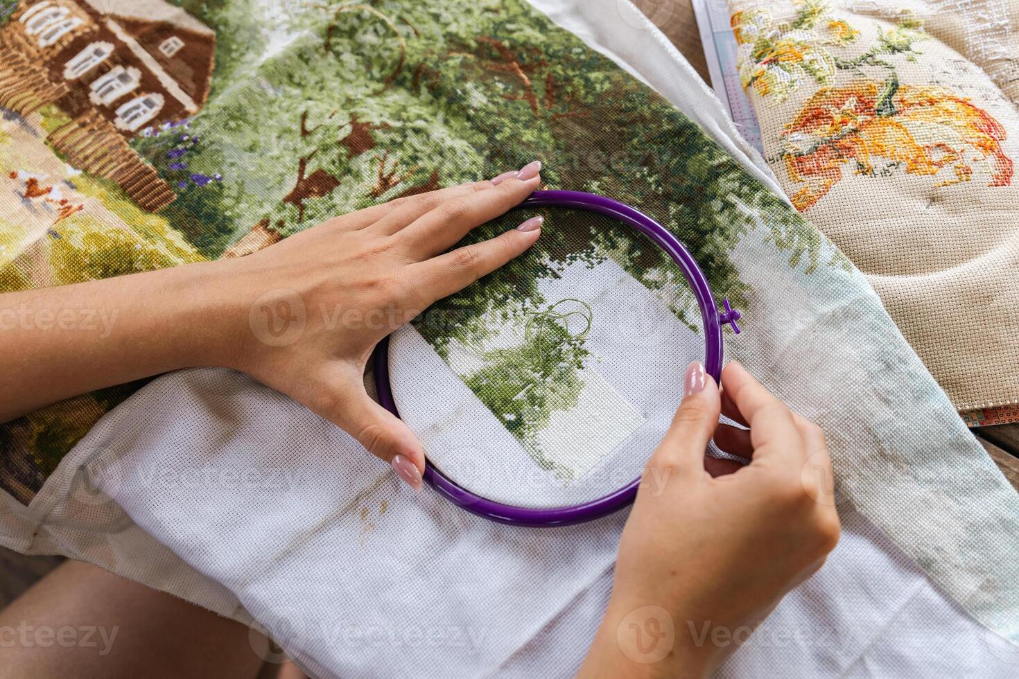 The image shows a person working on a cross-stitch embroidery project. They are using an embroidery hoop to hold the fabric taut and are carefully guiding the needle through the cloth. Hobbies. photo