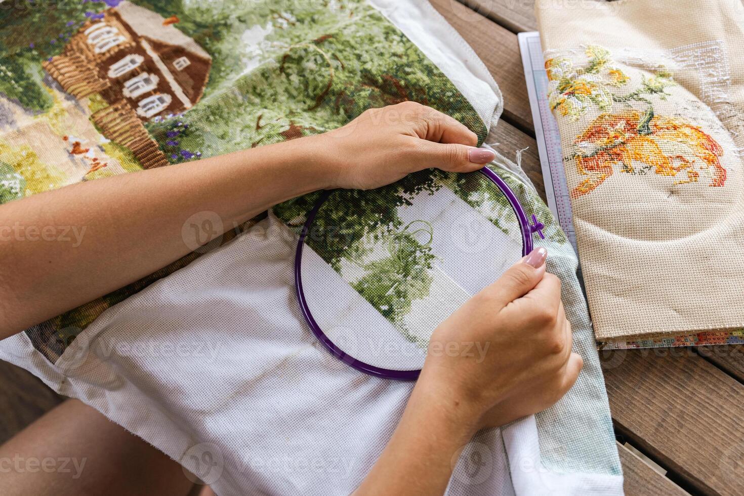 The image shows a person working on a cross-stitch embroidery project. They are using an embroidery hoop to hold the fabric taut and are carefully guiding the needle through the cloth. Hobbies. photo