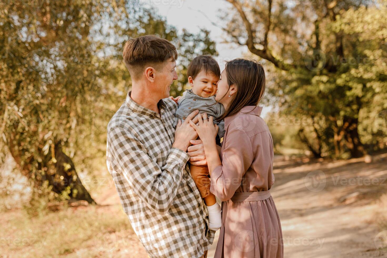 Happy family walking on the road in the park. Father, mother holding baby son on hands and going together. Rear view. Family Ties concept. photo