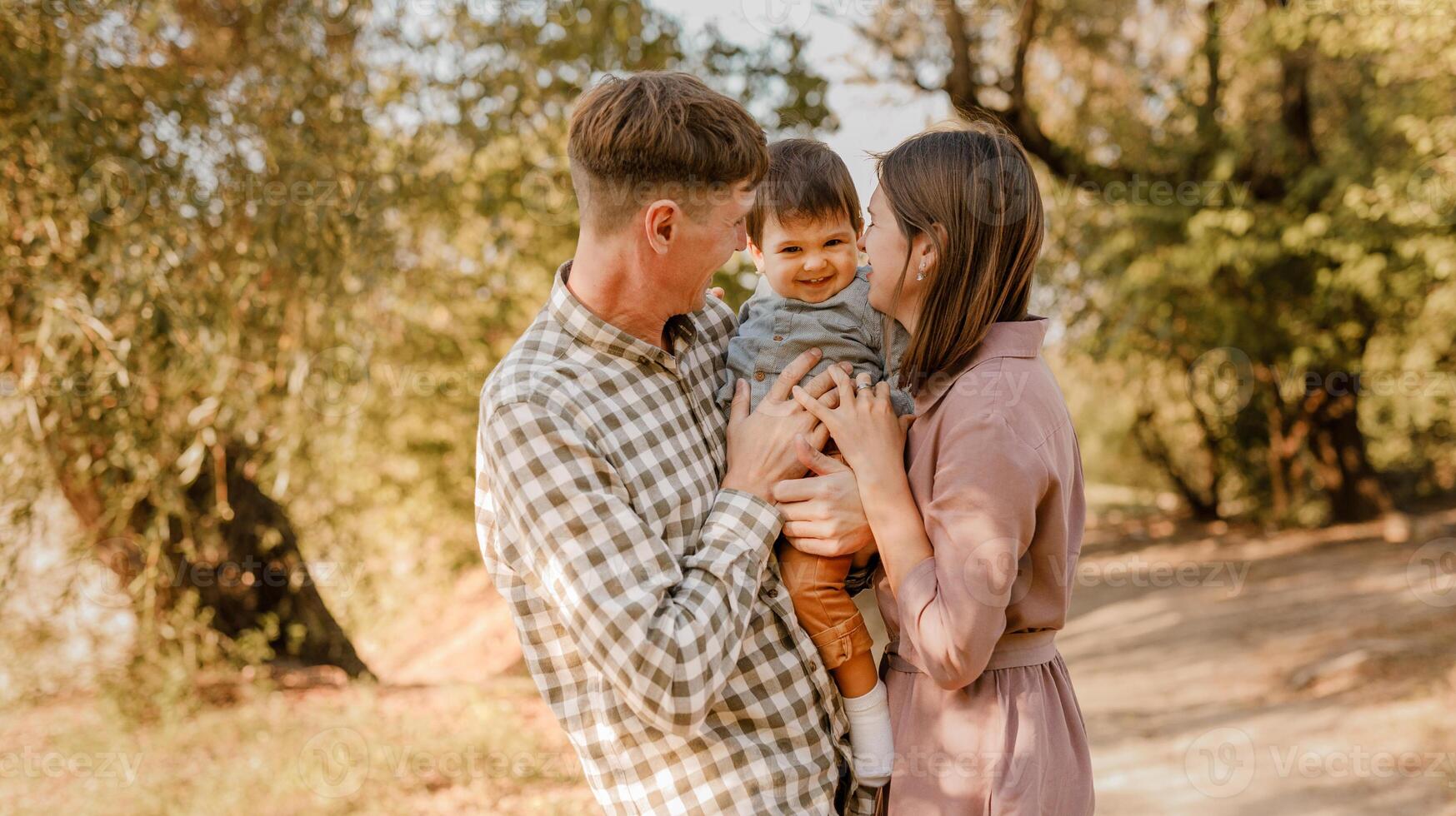 Happy family walking on the road in the park. Father, mother holding baby son on hands and going together. Rear view. Family Ties concept. photo