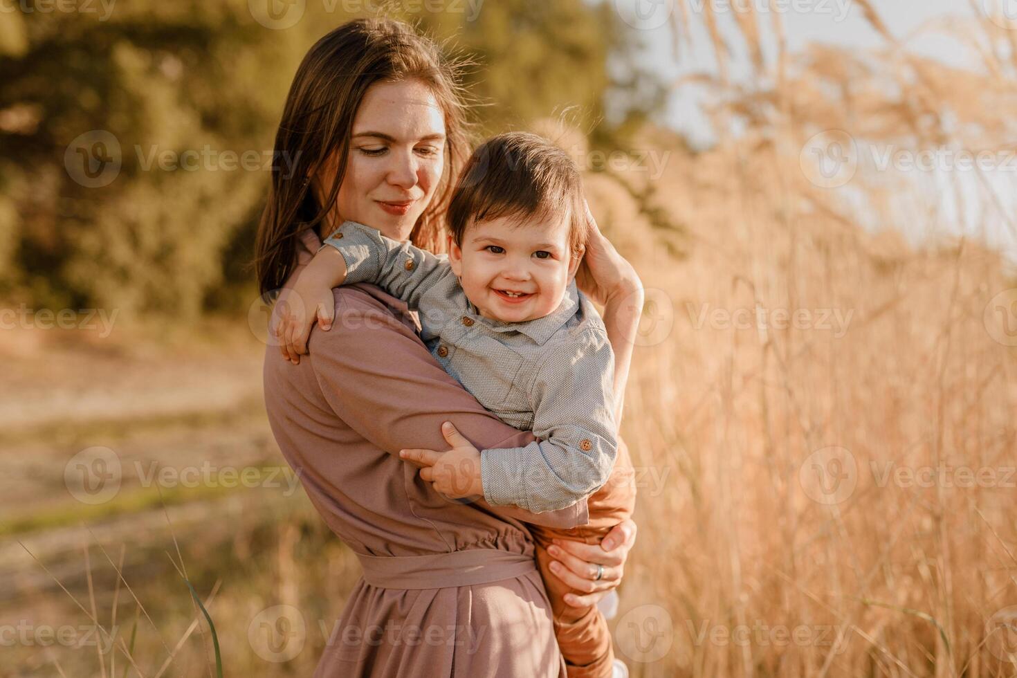 Portrait of happy loving mother hugging her baby son in the sunny park near river photo