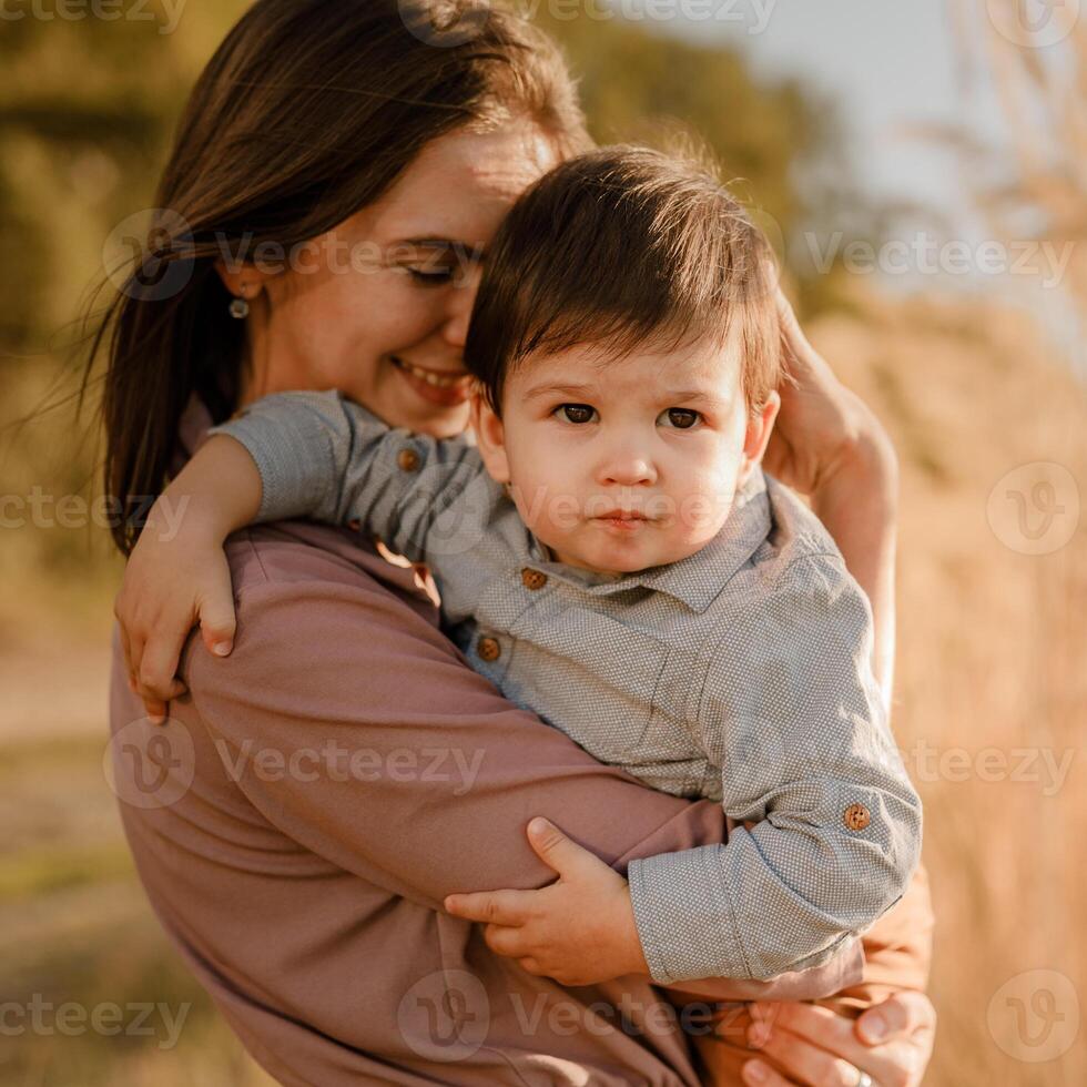 Portrait of happy loving mother hugging her baby son in the sunny park near river photo
