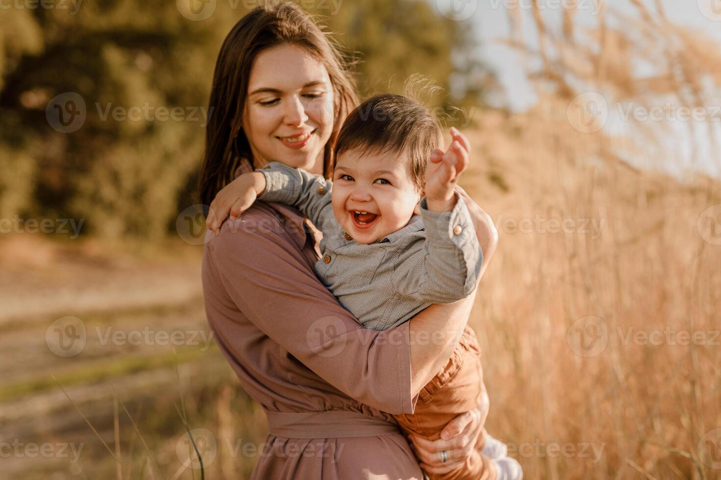 Portrait of happy loving mother hugging her baby son in the sunny park near river photo
