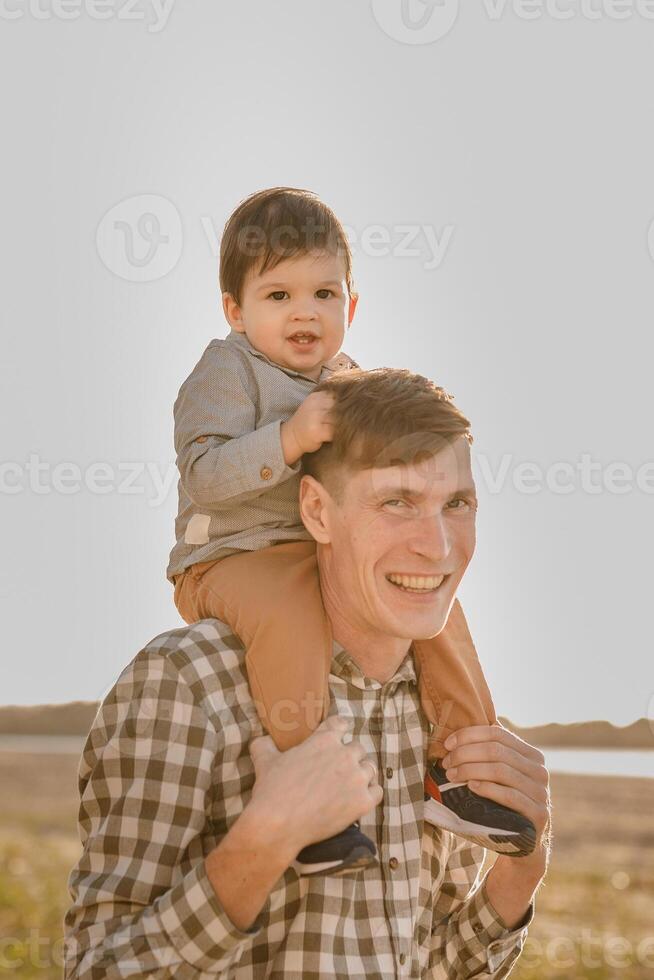 A child on his fathers neck. Walk near the water. Baby and dad against the sky photo