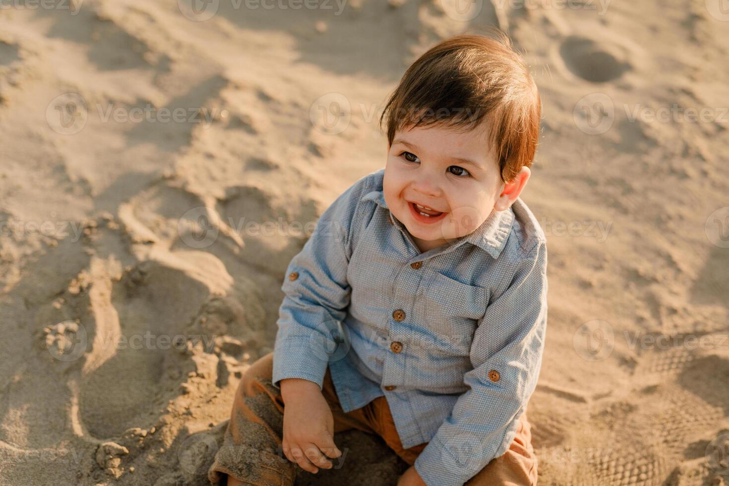 One-year-old boy sitting in the sand, smiling and playing photo