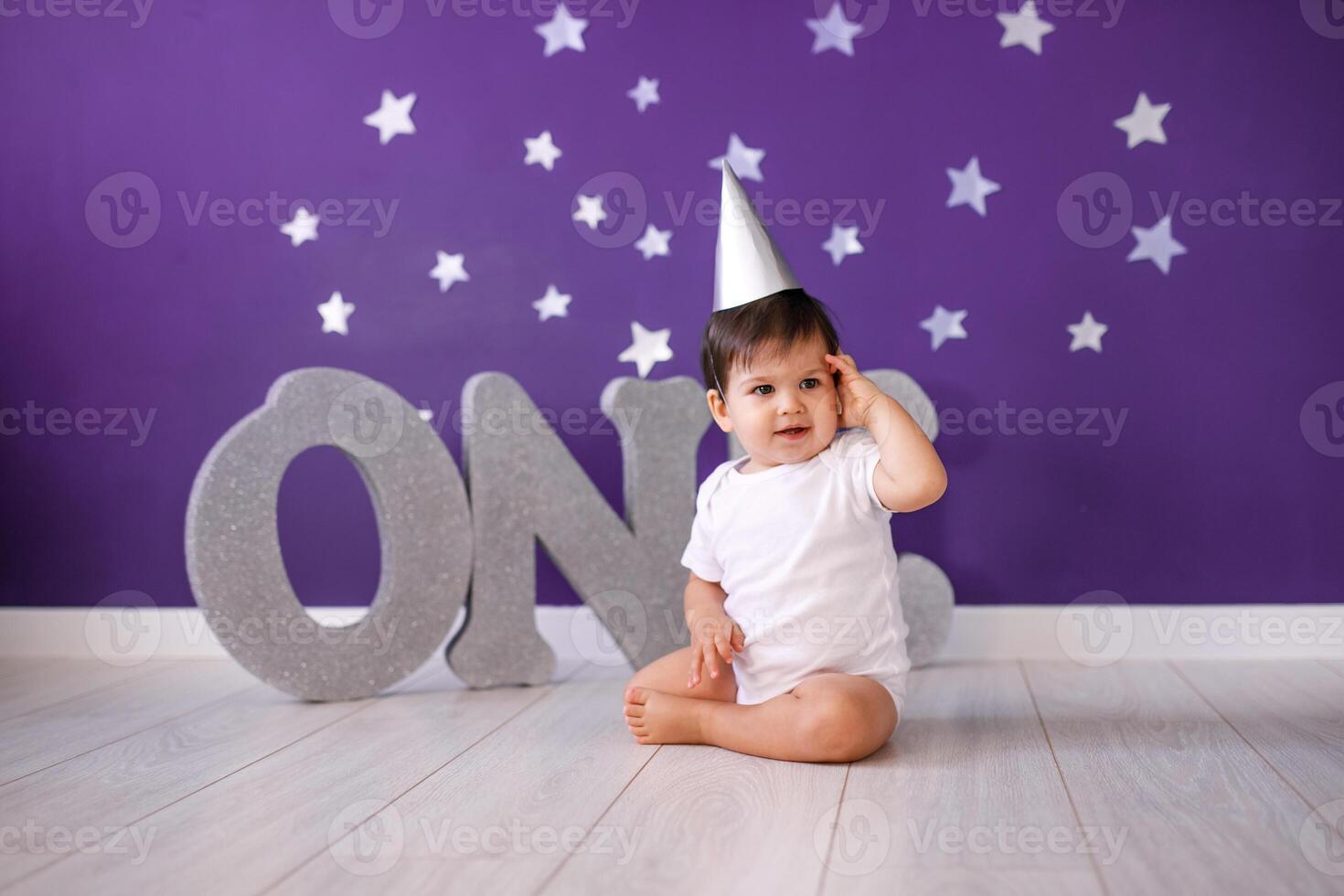 One year old baby boy celebrates birthday near silver letters ONE on blue background with stars photo