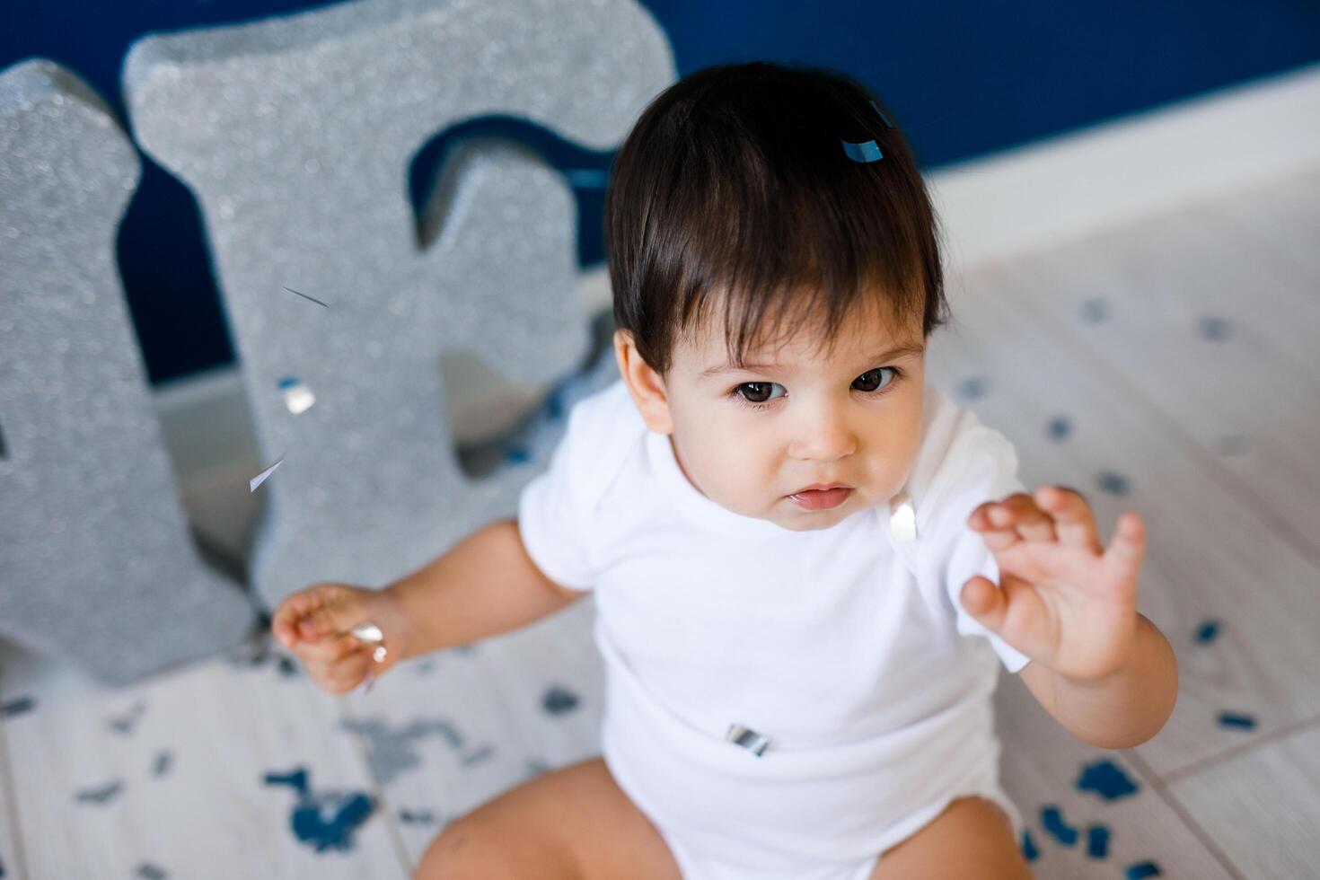 One year old baby boy celebrates birthday near silver letters ONE on blue background with stars photo