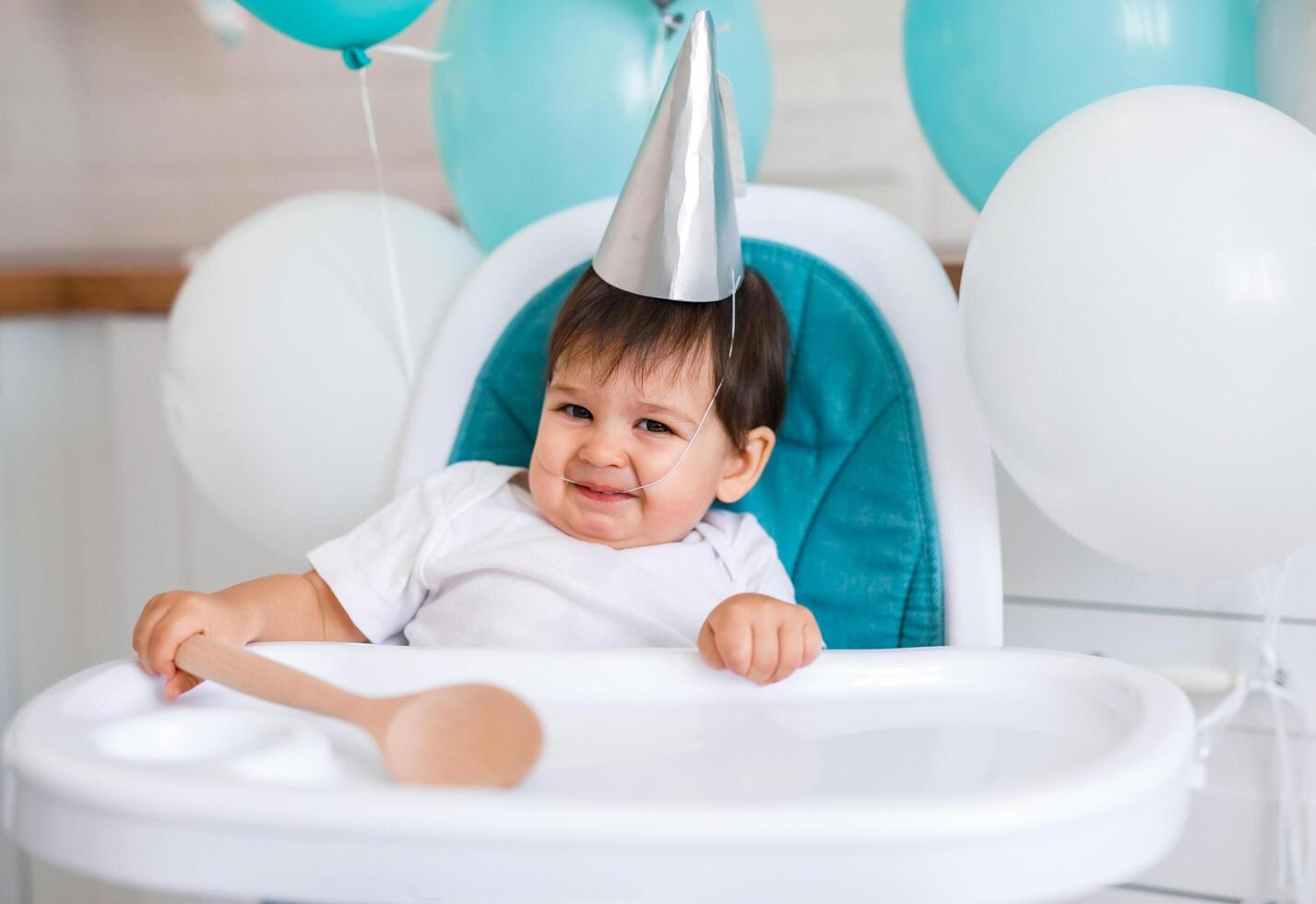 Little baby boy sitting in high chair at home on white kitchen and drinking water from sippy cup photo