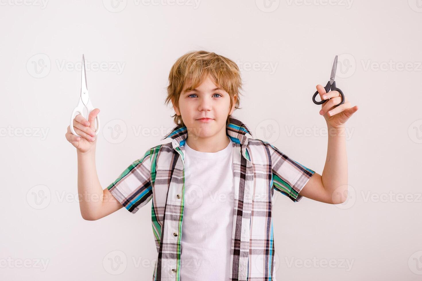 Happy blonde boy European appearance in a white shirt holding scissors on a white background photo