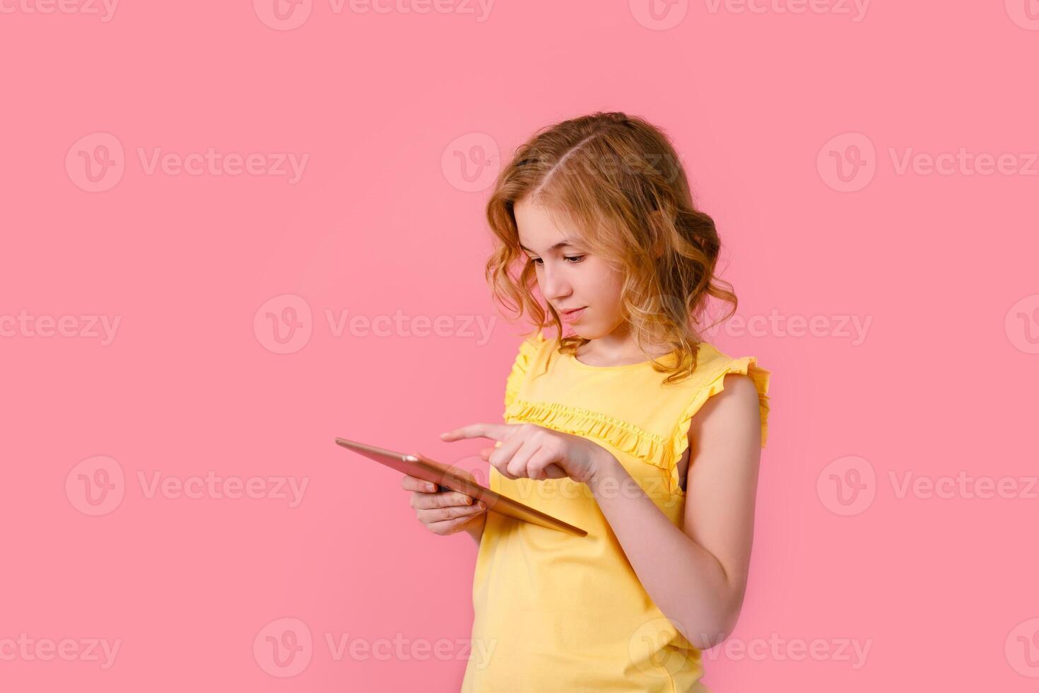 A teenage girl does her homework on a tablet. The student works and communicates with friends. Isolate on a pink background photo