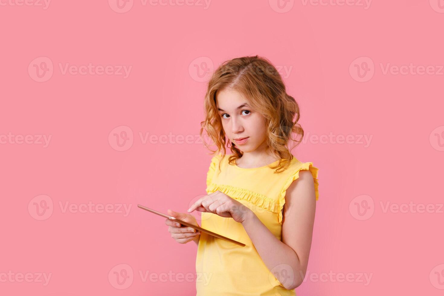 A teenage girl does her homework on a tablet. The student works and communicates with friends. Pink background with free space photo