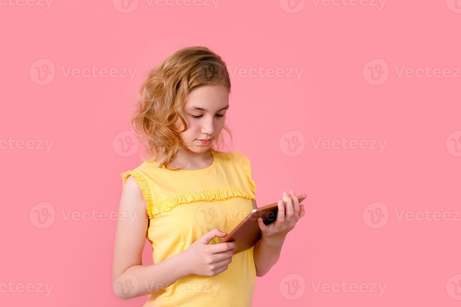A teenage girl does her homework on a tablet. The student works and communicates with friends. Isolate on a pink background photo