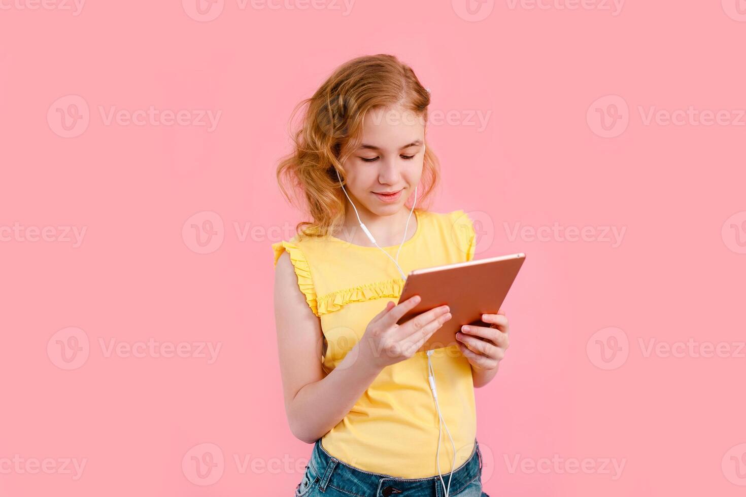A teenage girl does her homework on a tablet. The student works and communicates with friends. Pink background with free space photo