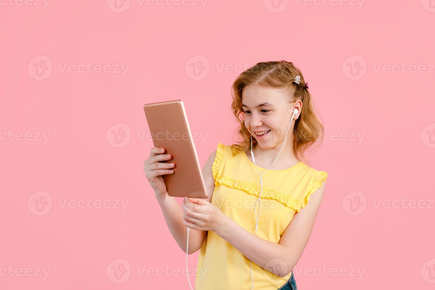 A teenage girl does her homework on a tablet. The student works and communicates with friends on Pink background photo