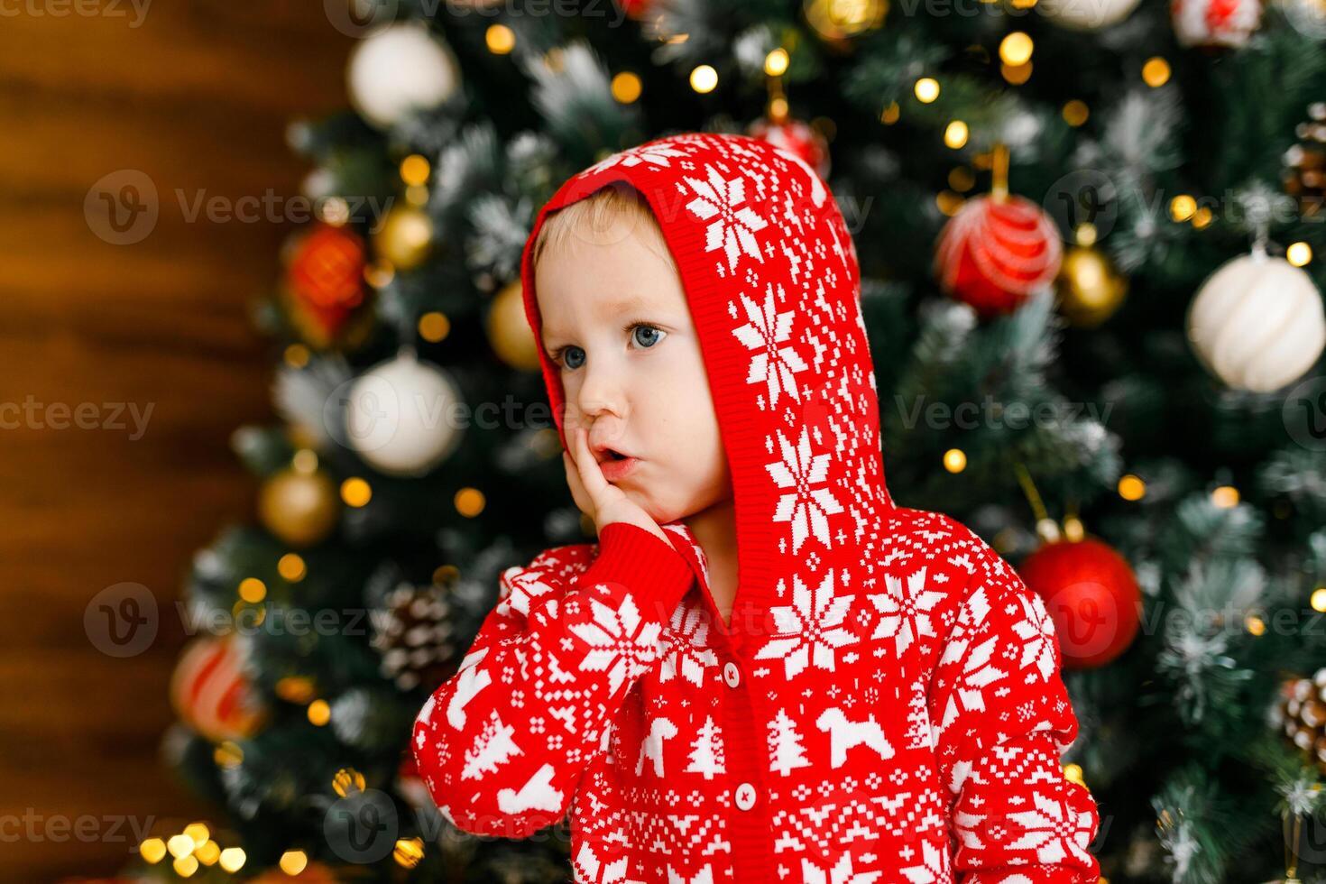 close-up portrait of toddler in red outfit with cute expressions of surprise and joy on background of Christmas tree photo