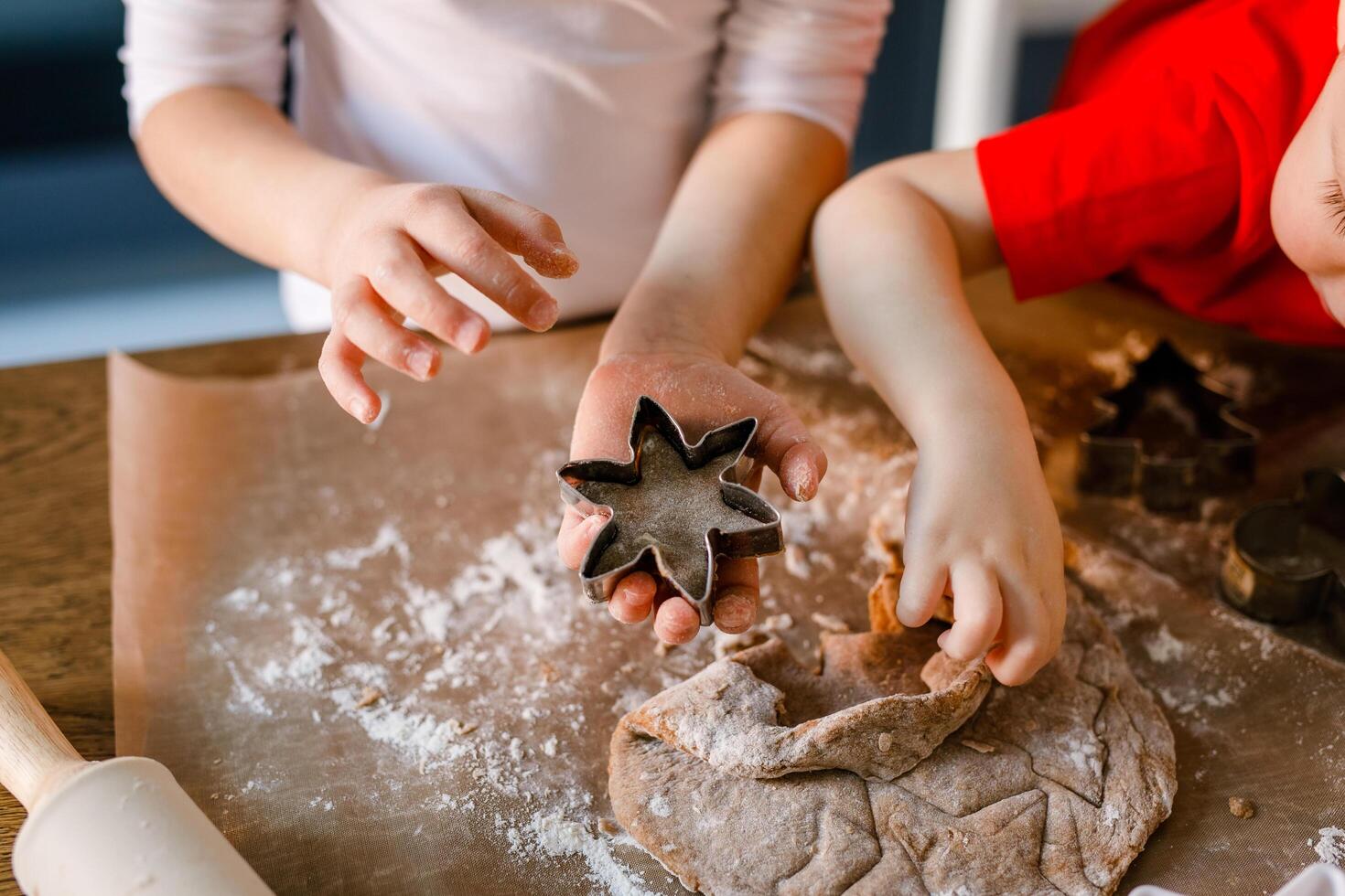 Close-up of children's hands cutting cookies with a cookie cutter on gingerbread dough photo