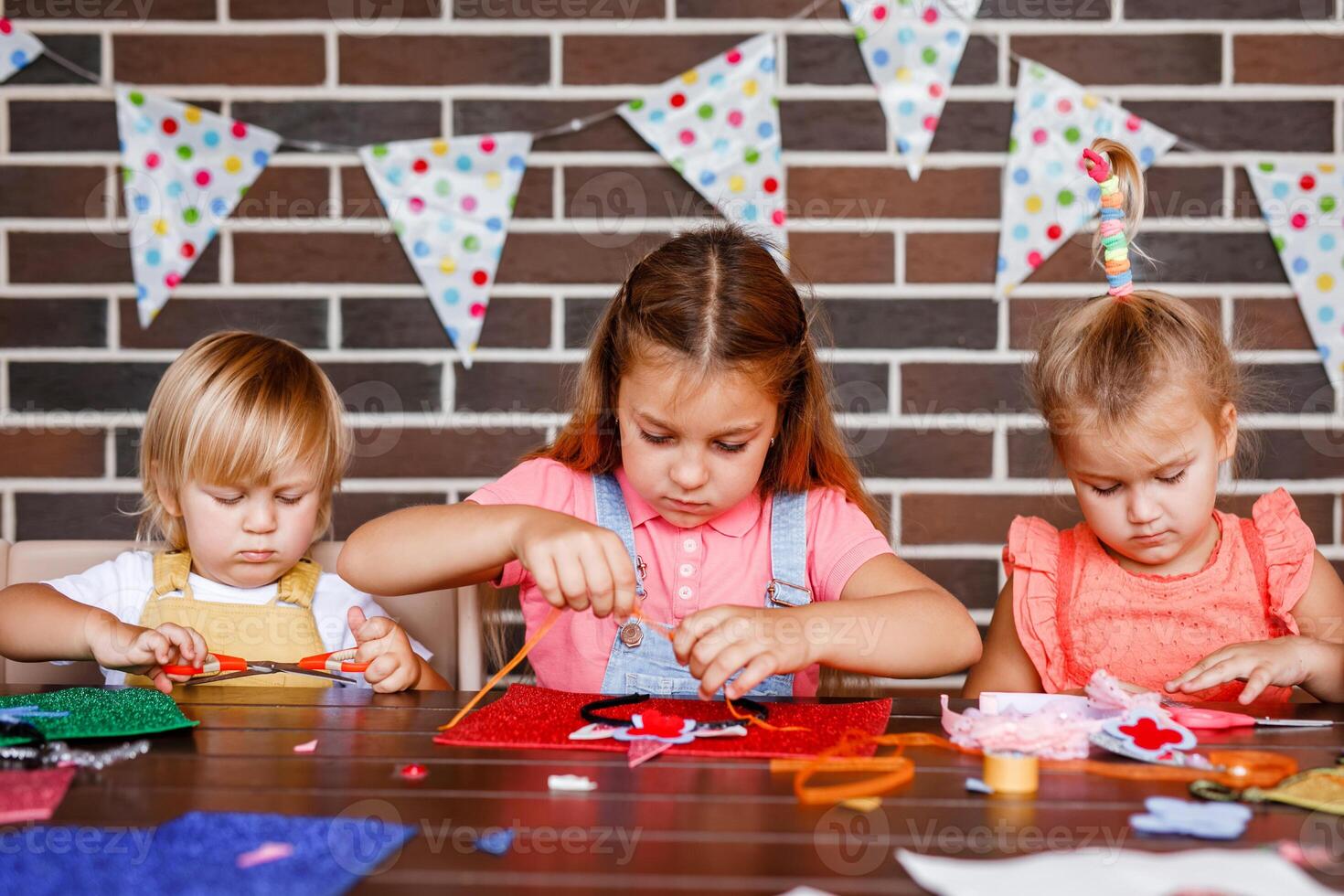 A little toddler boy and two girls cutting something out of beautiful paper at a party photo