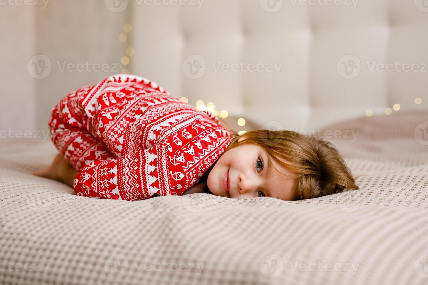 A girl in a Christmas pajama is lying on the bed and smiling photo