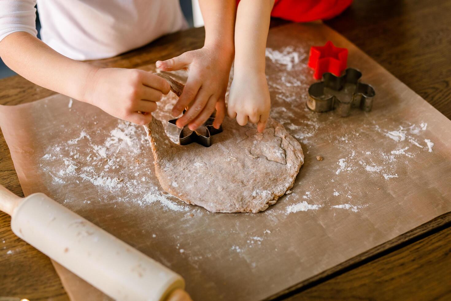 Close-up of children's hands cutting cookies with a cookie cutter on gingerbread dough photo