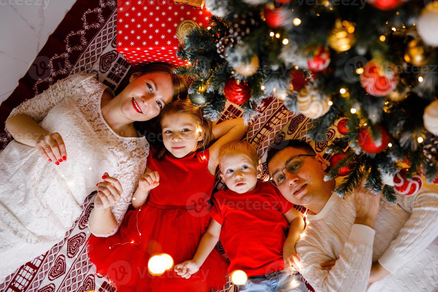 happy family of parents and girl with boy are lying together under the Christmas tree, smiling, seen from above photo