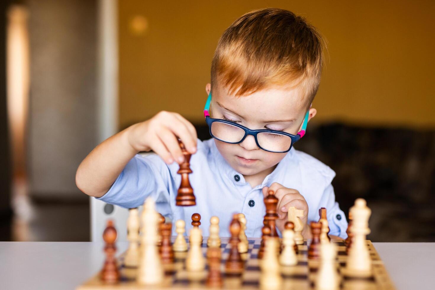 Ginger boy with down syndrome with big glasses playing chess at home photo