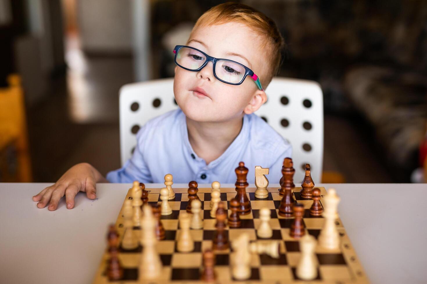 Ginger boy with down syndrome with big glasses playing chess at home photo