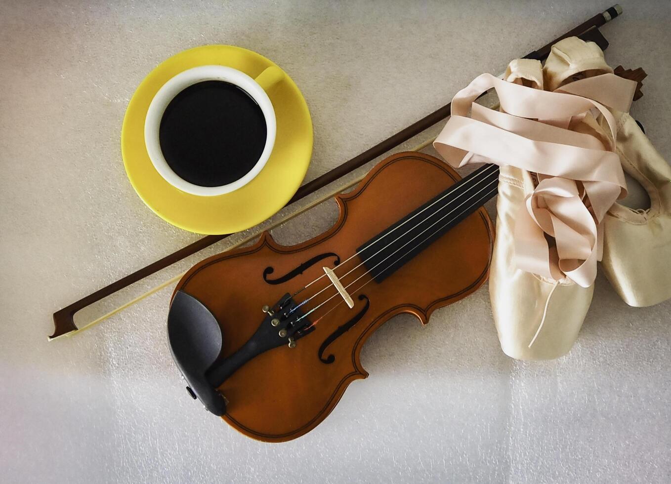 Ballet shoes and violin put beside yellow ceramic coffee cup photo