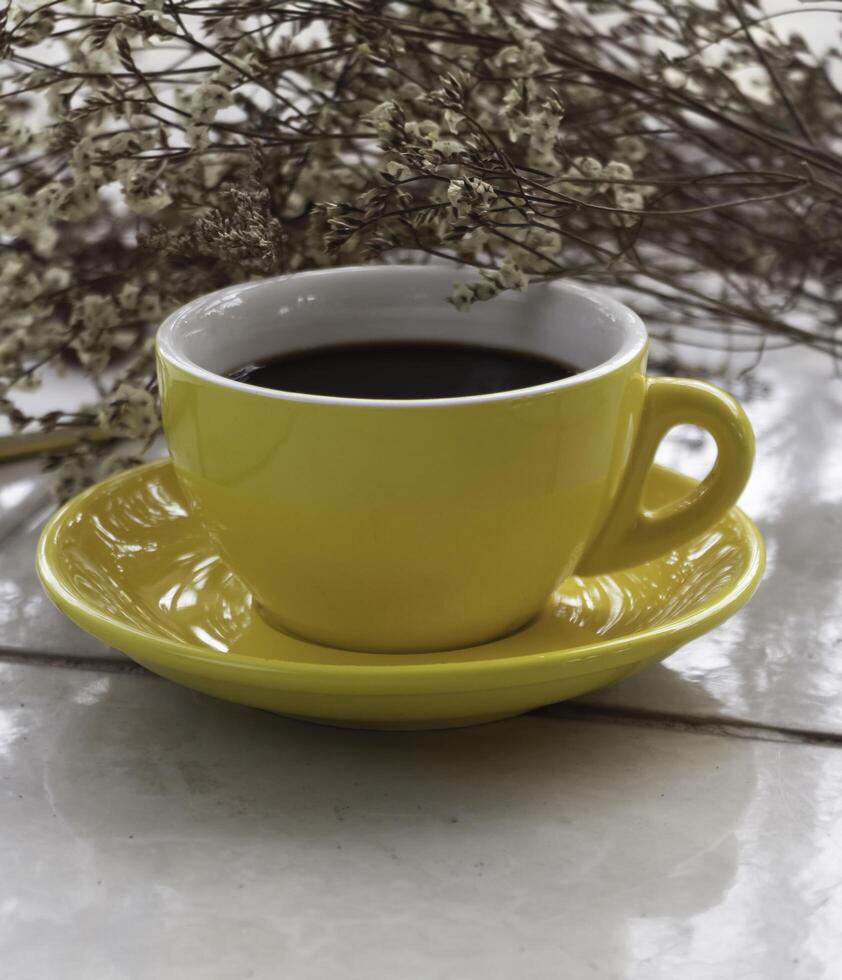 Yellow ceramic cup with black coffee put beside dried flower photo