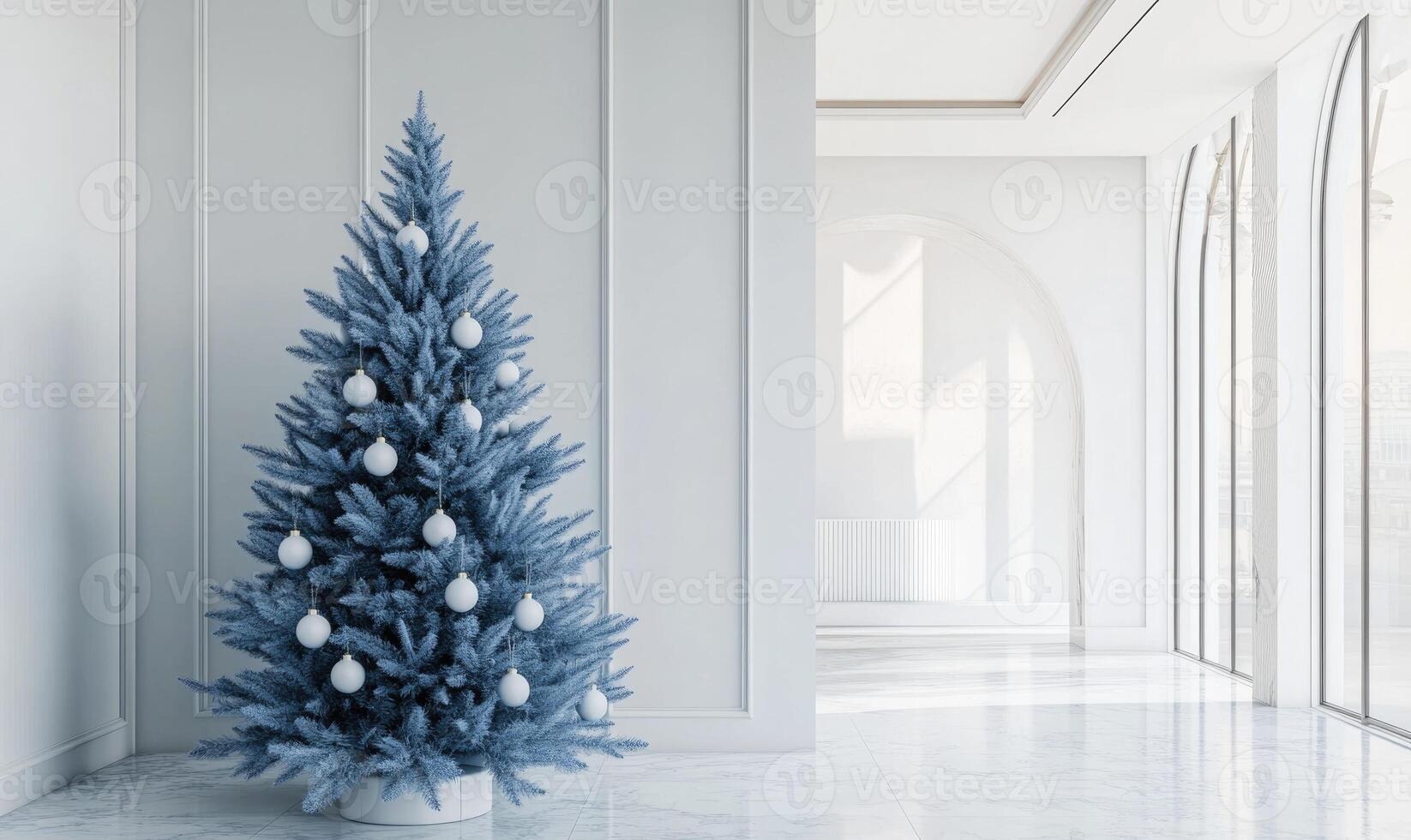 A blue Christmas tree with white ornaments sits in a large, empty room photo