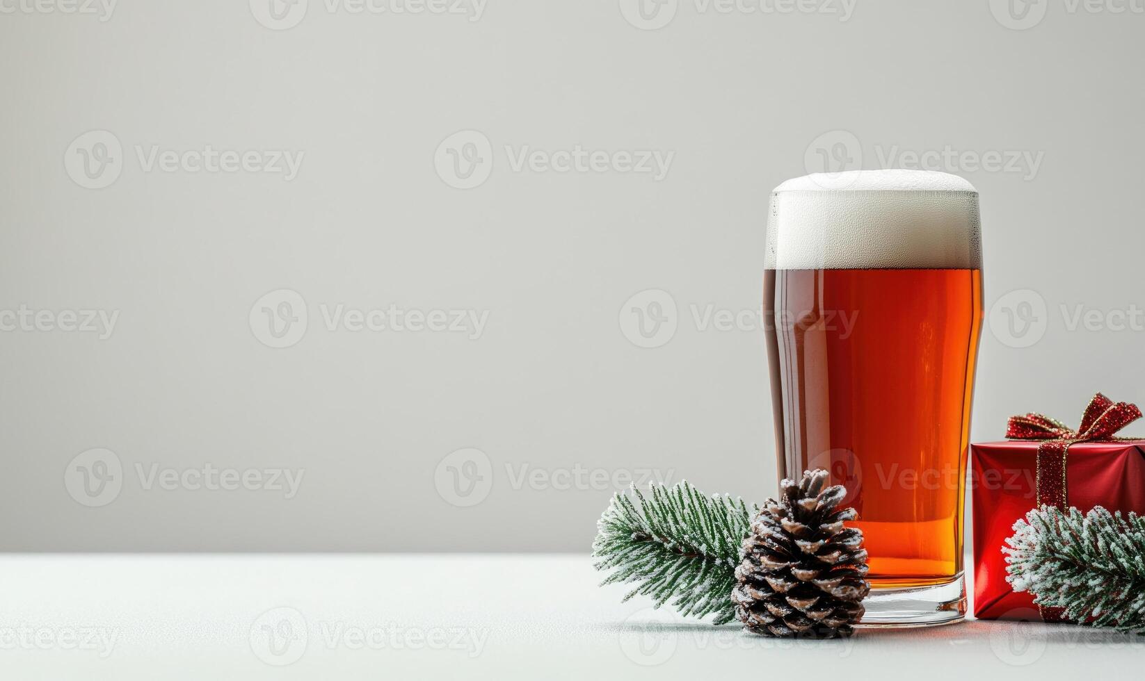 A glass of beer sits on a table next to a pine cone and a red gift box photo