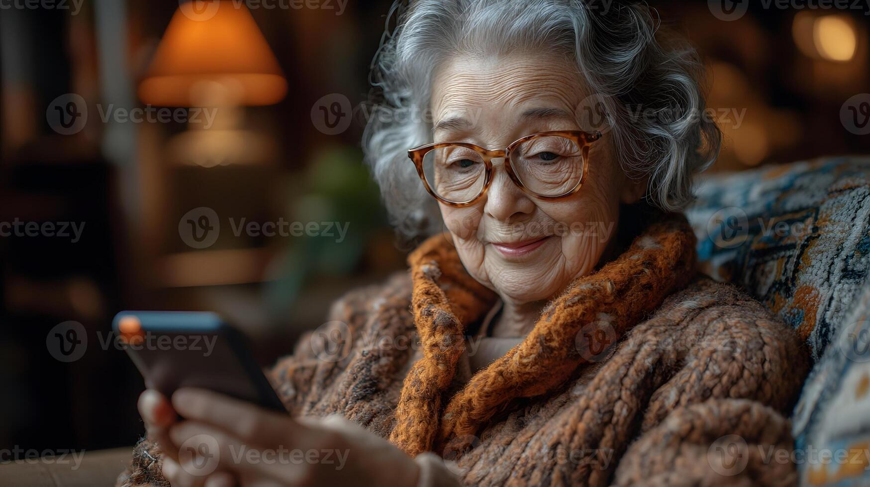 Smiling elderly woman seated on a sofa, holding her phone and reading a message. The soft light in the room creates a warm, peaceful atmosphere. photo