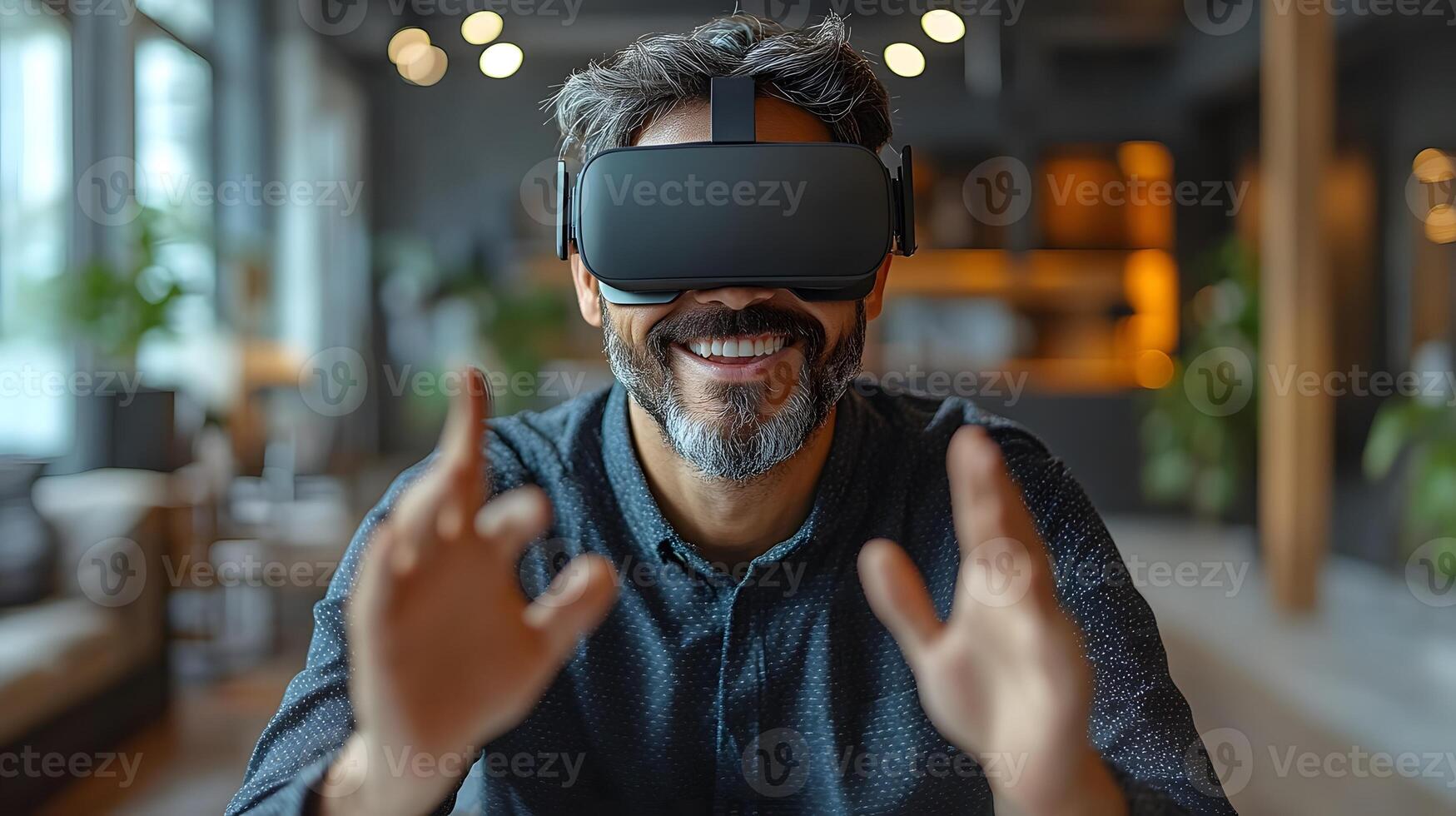 A businessman with a cheerful expression wearing virtual reality goggles, sitting at his desk in a modern office, making creative hand gestures. photo