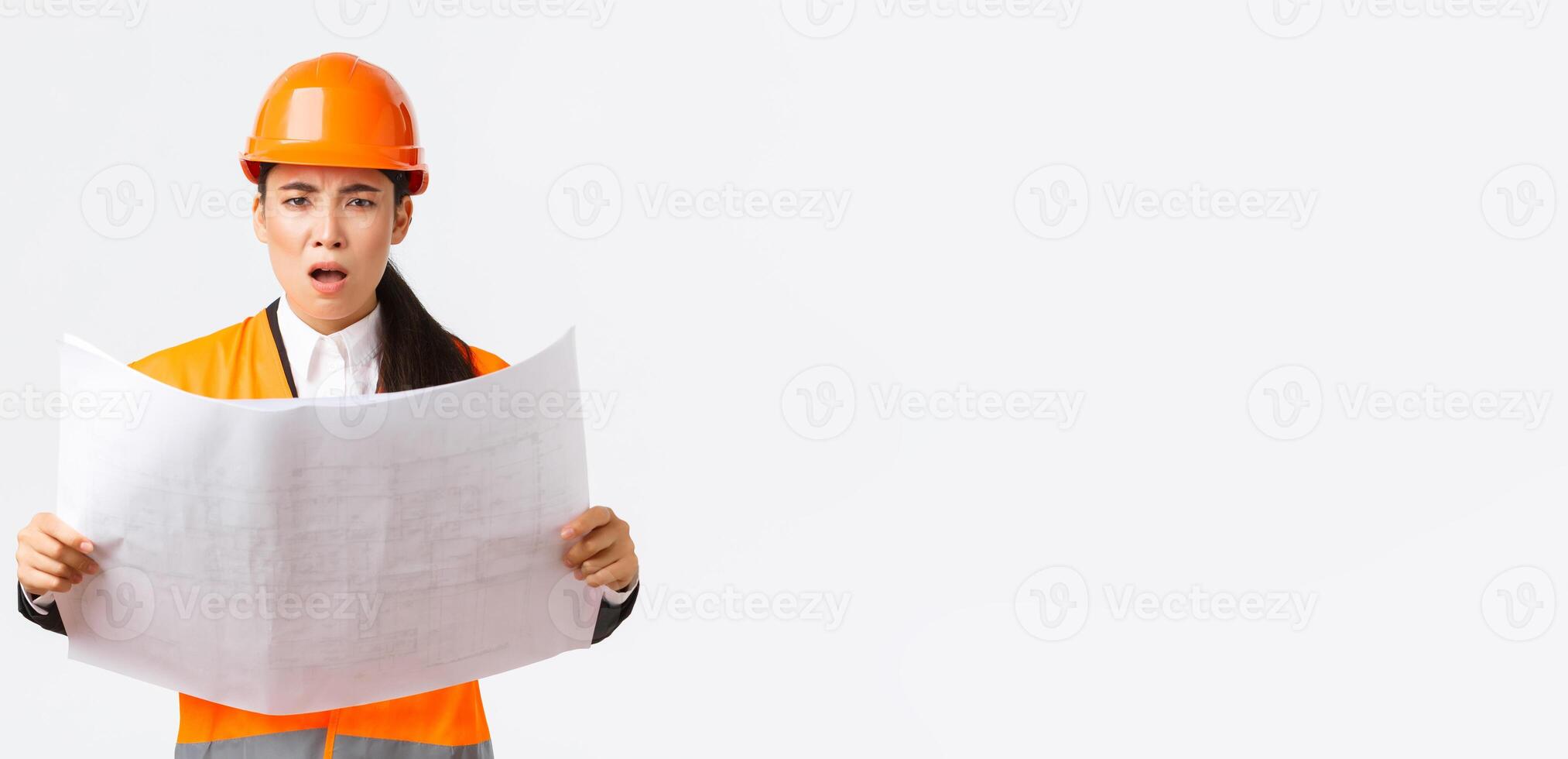 Frustrated and displeased female asian engineer, chief architect at construction zone, looking disappointed after studying blueprints, stare camera, scolding manager, white background photo
