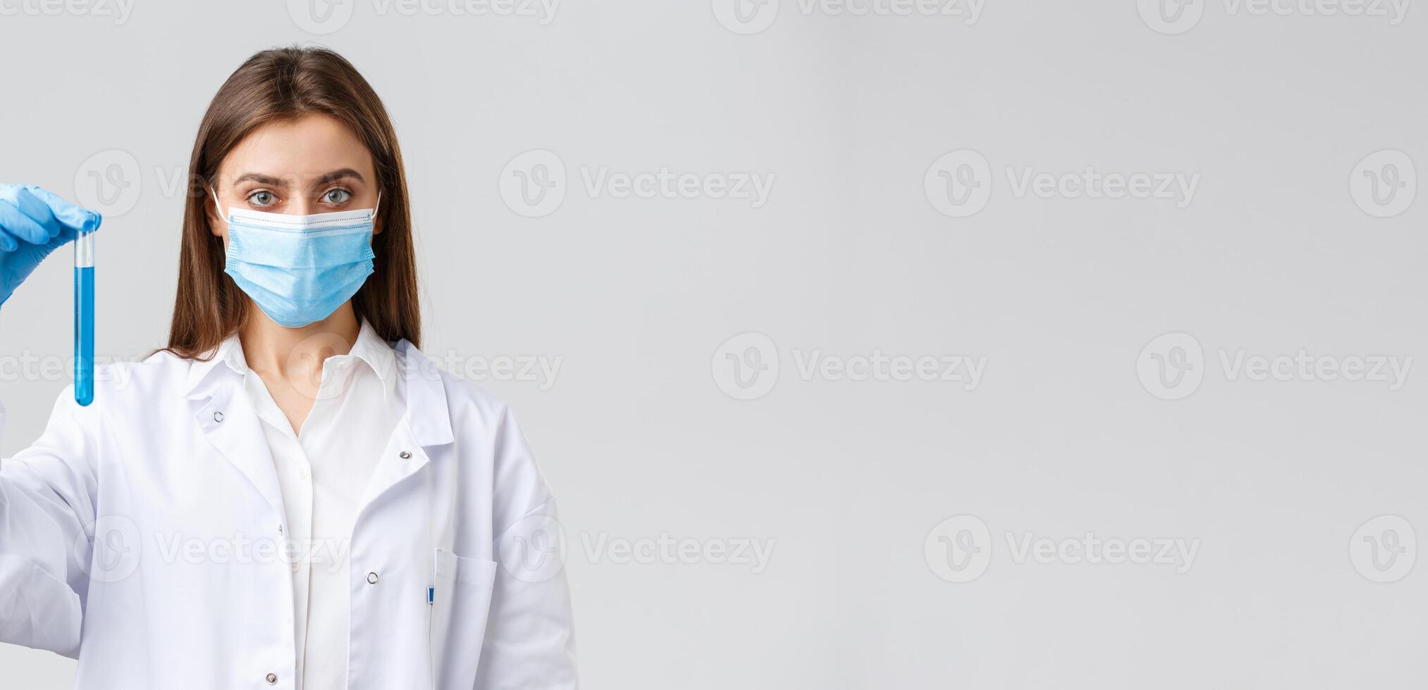 Covid-19, preventing virus, healthcare workers and quarantine concept. Determined female doctor or nurse in medical mask and scrubs, showing test-tube with coronavirus vaccine photo