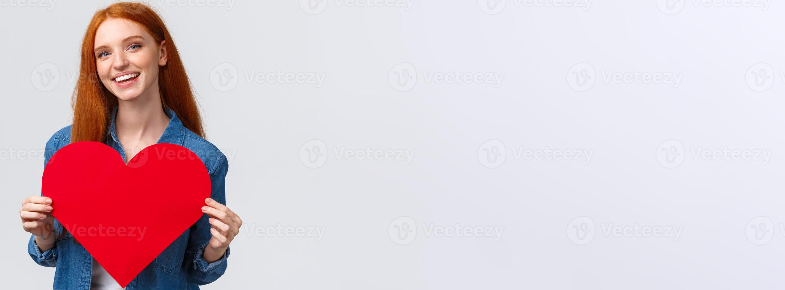 Valentines day, romance and teenagers concept. Lovely and cute redhead girlfriend asking wanna go prom together with big red heart, confessing love, smiling joyfully, white background photo