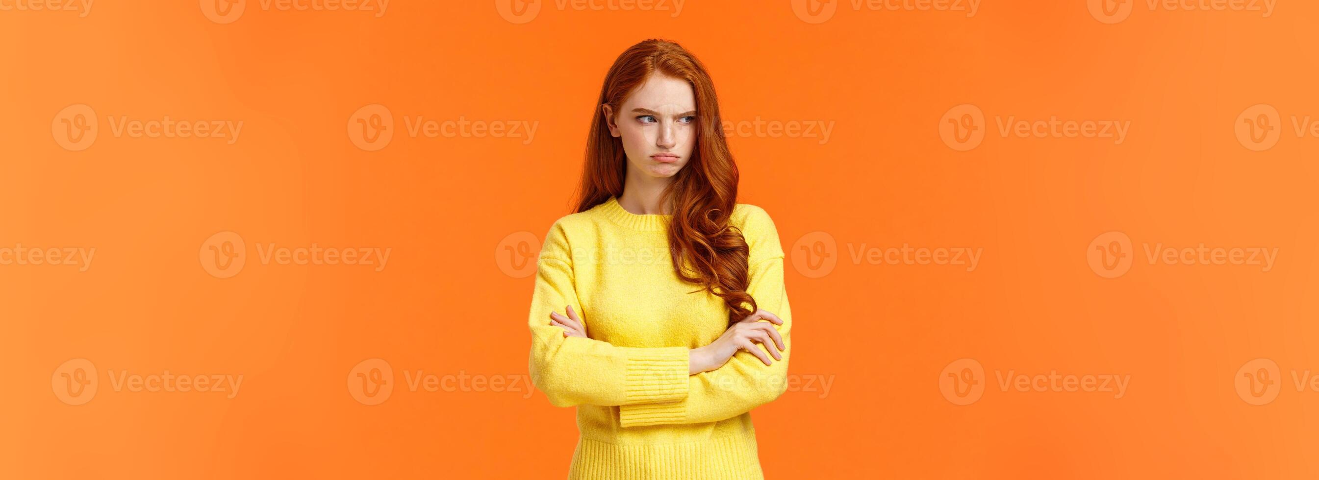 Offended angry and tensed woman with curly red hair, freckles, having bad mood, cross arms chest, thinking troublesome situation, frowning getting mad, standing orange background distressed photo